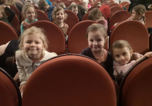 Widok na trzy dziewczynki siedzące na widowni w ŁDK. W tle widać dzieci zajmujące miejsca na widowni.